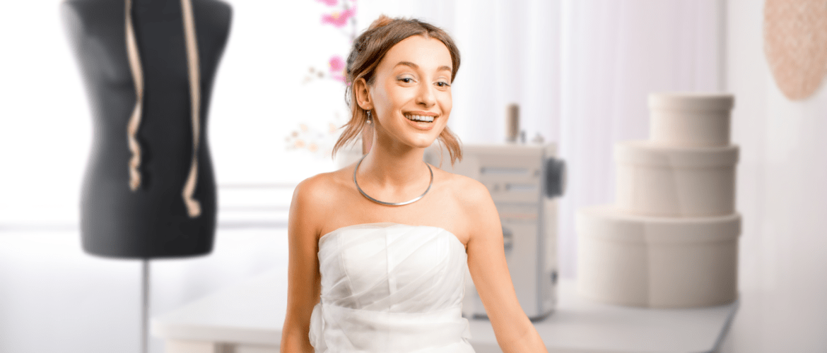 A young woman in a wedding dress standing in front of a sewing machine & mannequin.